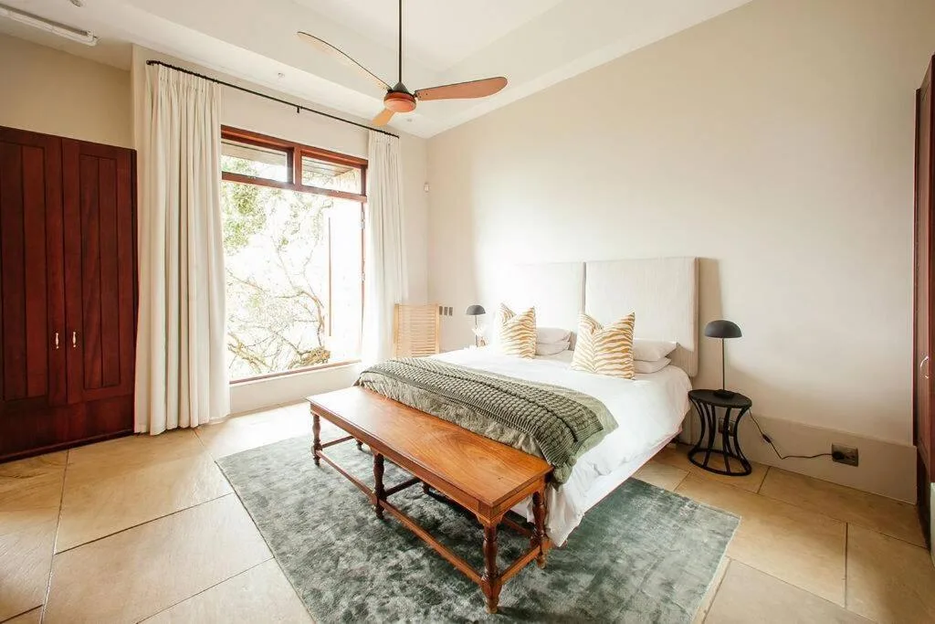 Spacious bedroom with queen bed, cream headboard, and large windows overlooking garden