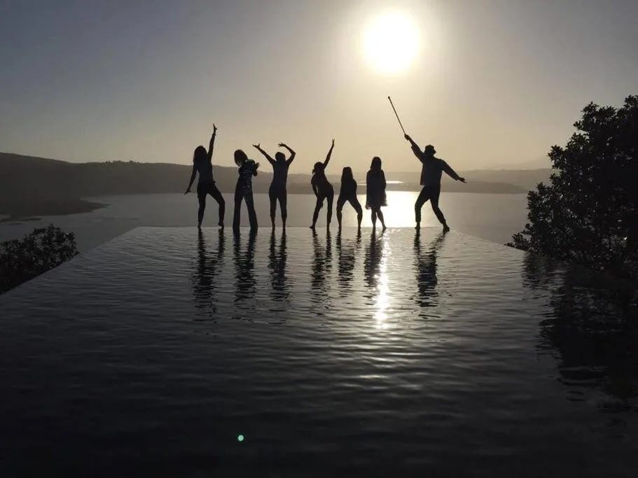 Group enjoying infinity pool overlooking scenic lagoon and distant mountains