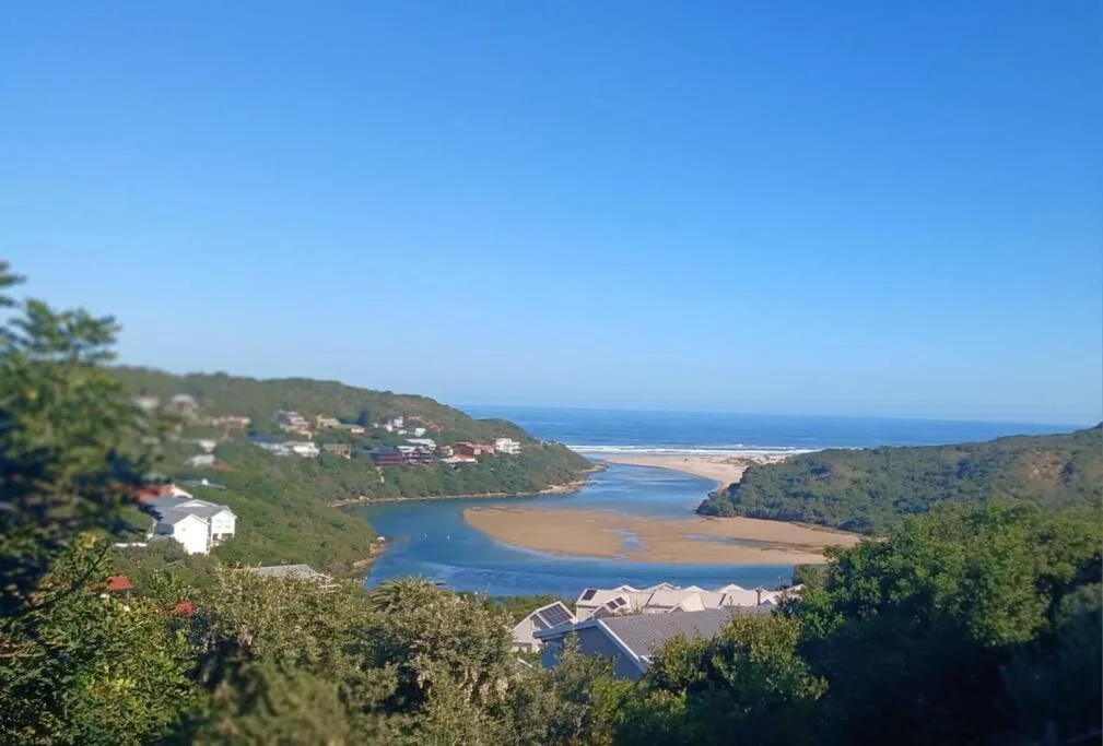 Coastal lagoon with sandy beaches and forested hills under blue sky