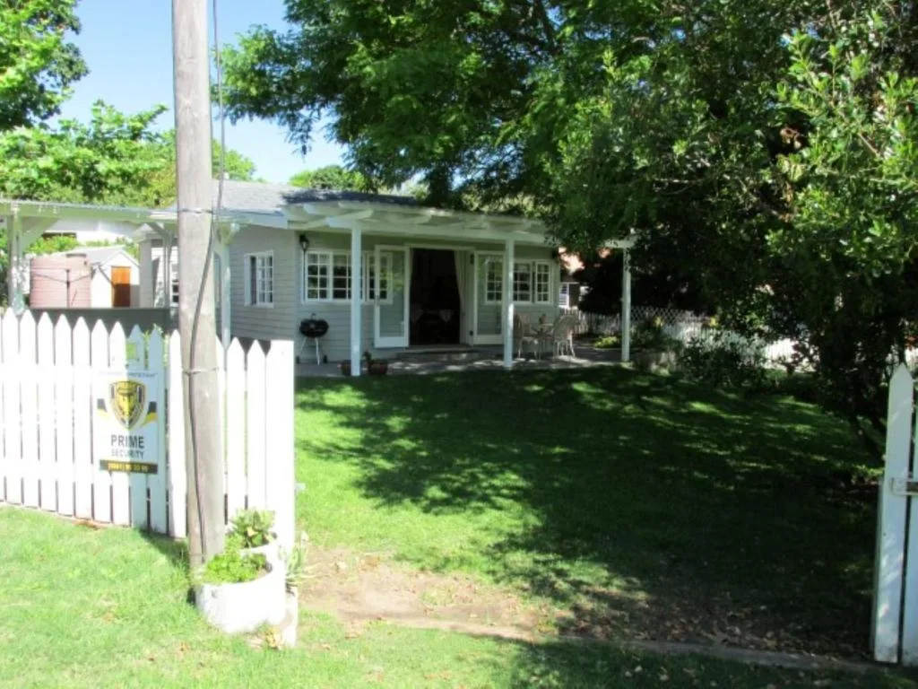 White cottage with covered porch, white picket fence, and mature trees