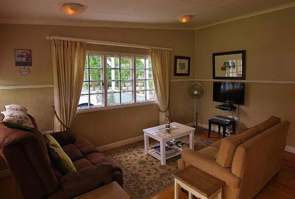 Warm lounge with burgundy sofa, armchairs, TV and large windows overlooking garden