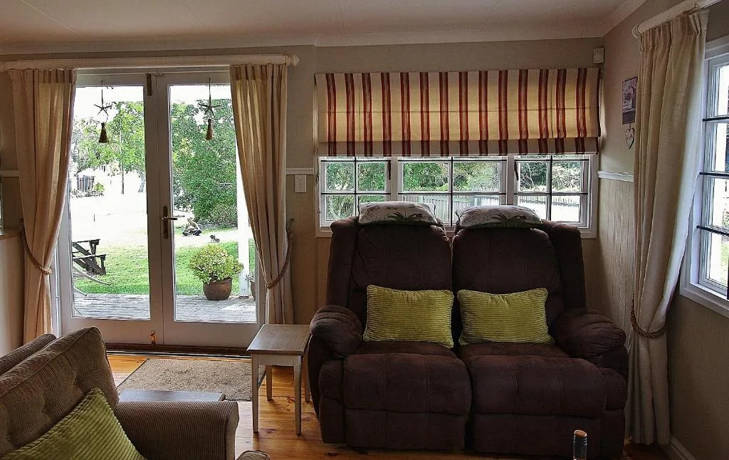 Spacious lounge with dark recliner sofa and green cushions facing garden view