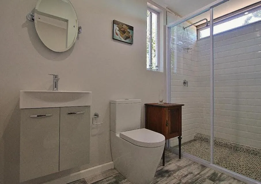 Modern bathroom with white vanity, toilet, mirror, and glass shower enclosure