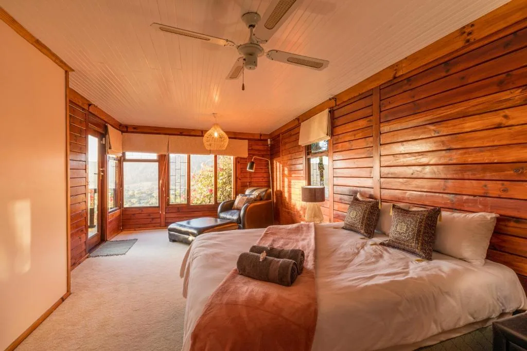 Spacious wooden bedroom with queen bed, lounge chair, and panoramic windows