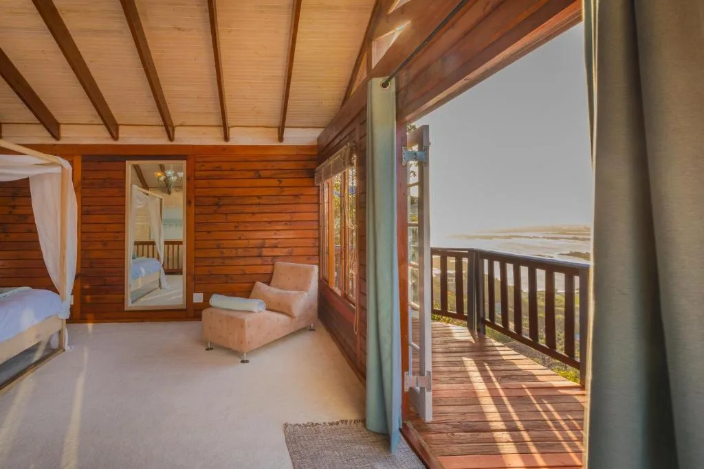 Spacious bedroom with wooden beams, four-poster bed, and lagoon view through open doors