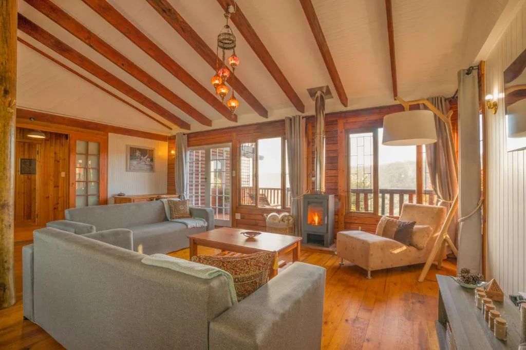 Spacious lounge with exposed wooden beams, fireplace, and panoramic windows overlooking mountains