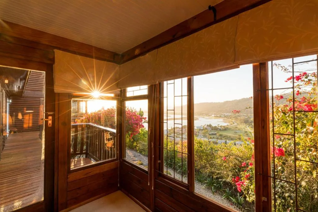 Panoramic lagoon and valley views through large wooden-framed windows at sunset