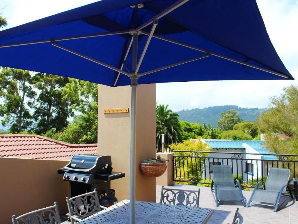 Shaded outdoor deck with blue umbrella, braai grill, and mountain views