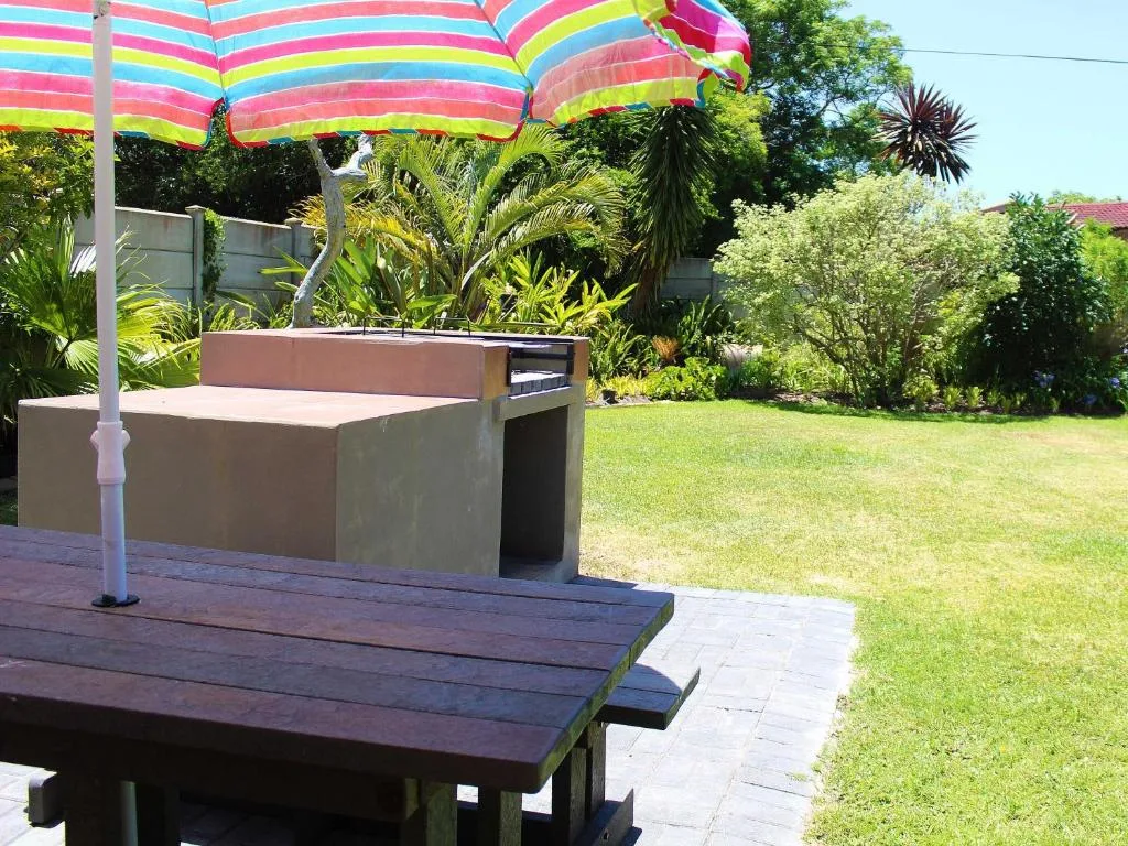 Outdoor braai area with colorful striped umbrella and wooden benches on garden patio