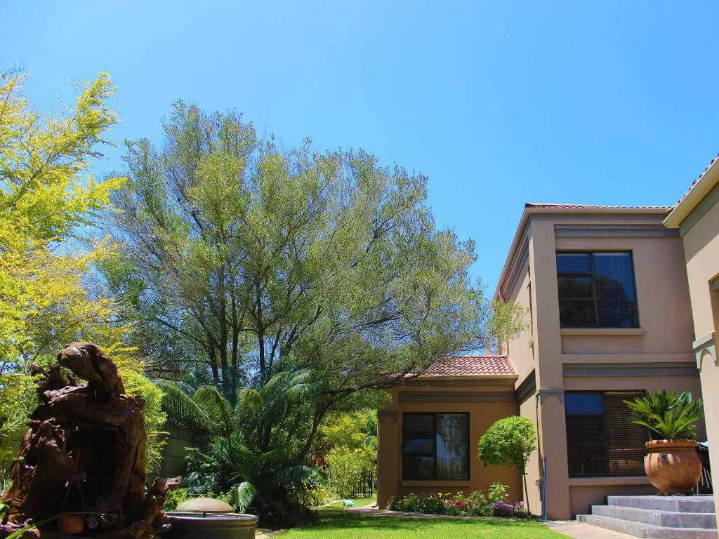 Modern house with manicured gardens and mature trees under clear sky