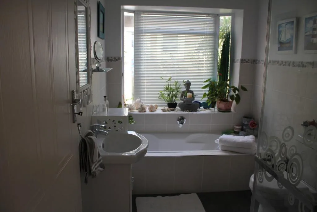 Bright bathroom with bathtub, sink, and window overlooking garden plants