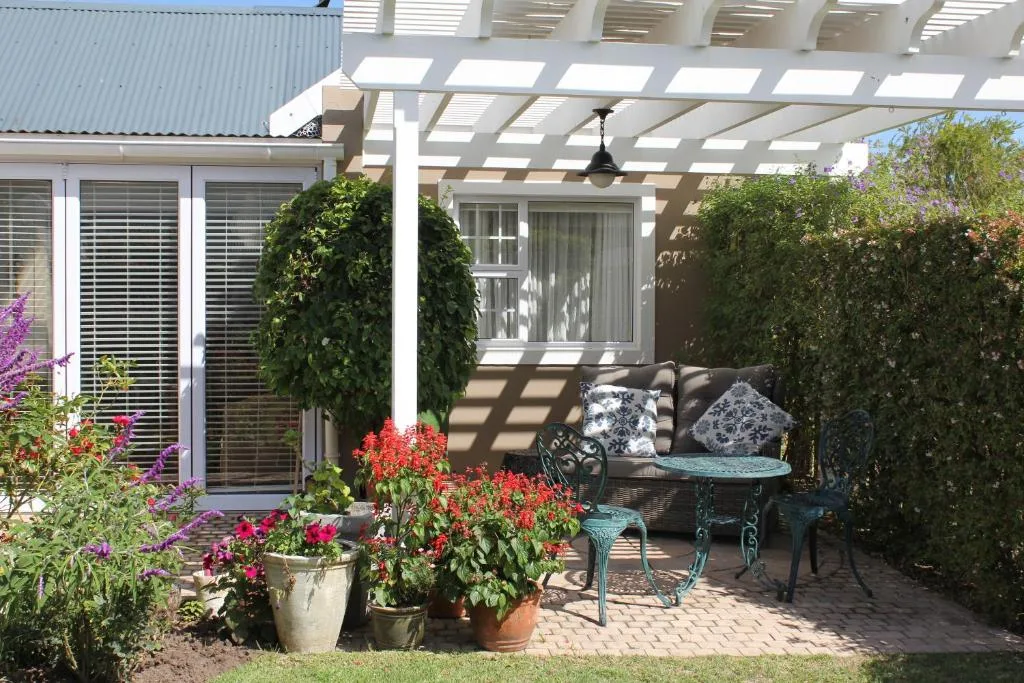 Covered patio with outdoor seating, potted flowers, and lush green hedges