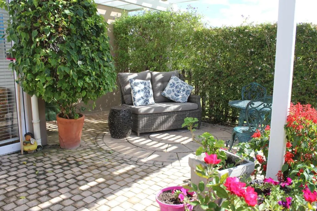 Covered patio with wicker seating, flowering plants, and hedge privacy screening