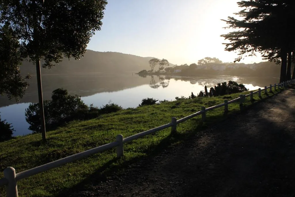 Tranquil lagoon vista with misty mountains, trees, and wooden fence