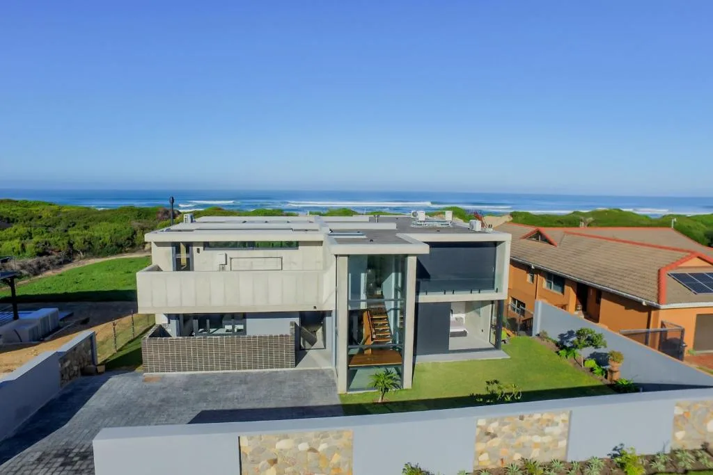 Modern coastal home with ocean and lagoon views beyond green lawns