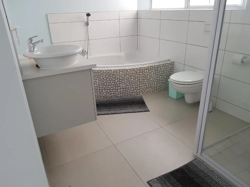 Modern bathroom with bathtub, pedestal sink, toilet, and tiled walls