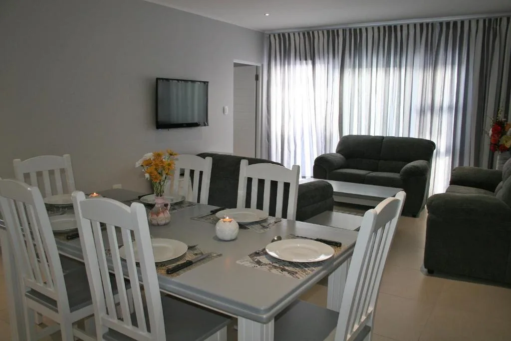 Dining table with white chairs, lounge area visible in background