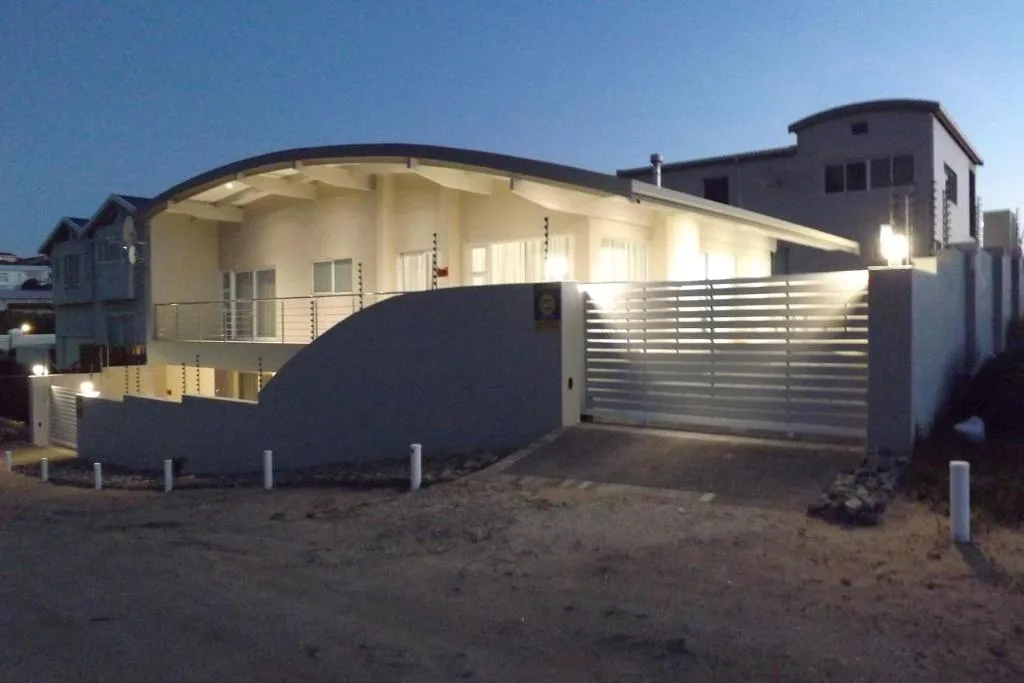 Modern curved beach house with illuminated facade and metal garage gates at dusk