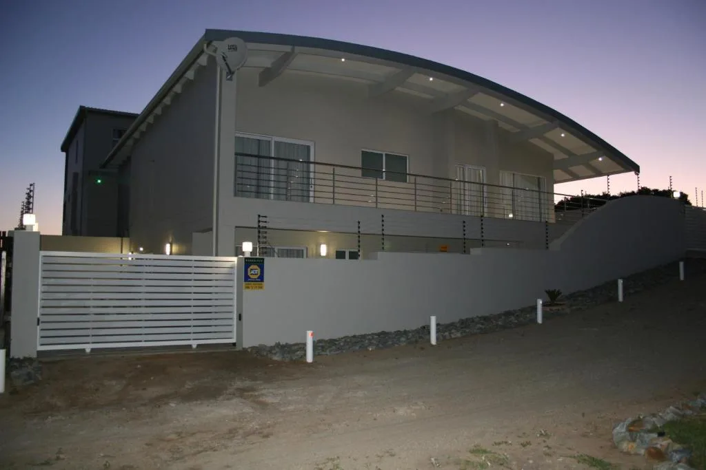 Modern white holiday apartment with covered deck and gated entrance at dusk