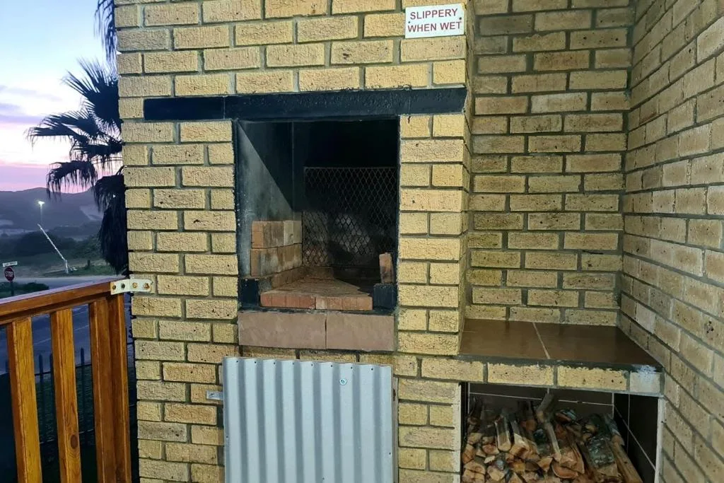 Outdoor braai fireplace with safety warning sign and firewood storage
