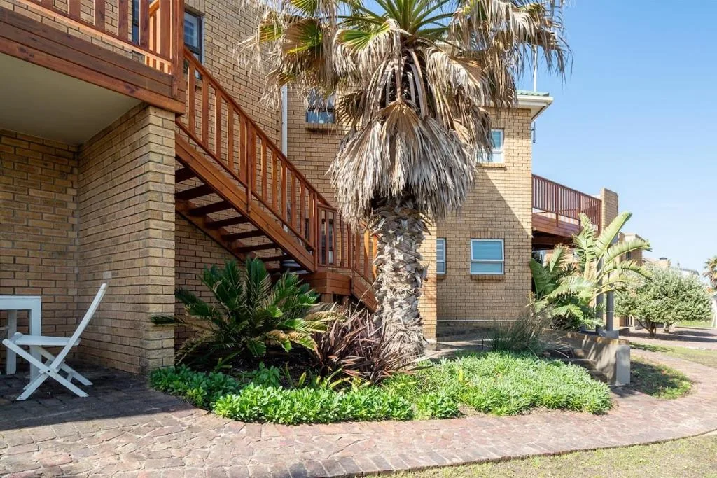 Brick holiday apartment with wooden deck stairs and palm tree garden