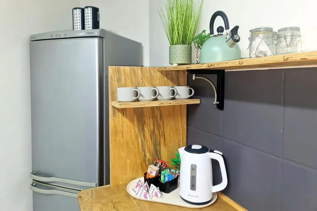 Modern kitchenette with stainless steel fridge, kettle, and wooden shelving