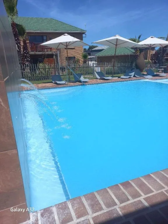 Bright blue swimming pool with white umbrellas and loungers beside brick building