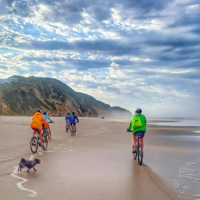 Scenic beach with cyclists and cliffs under dramatic cloudy sky