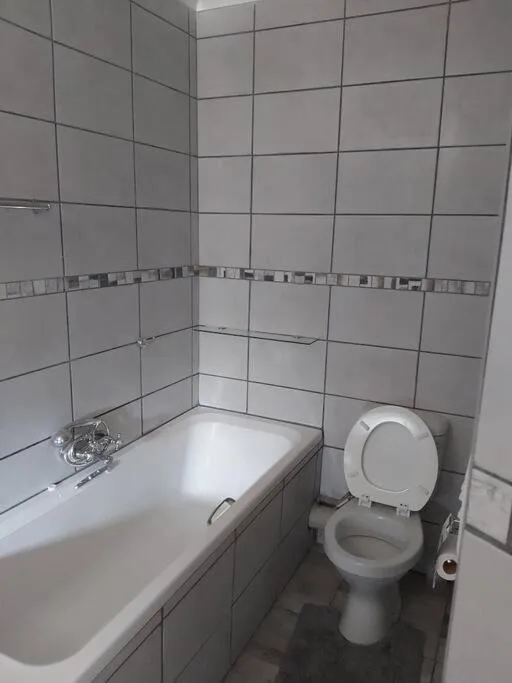 Clean bathroom with white bathtub, toilet, and gray tile walls
