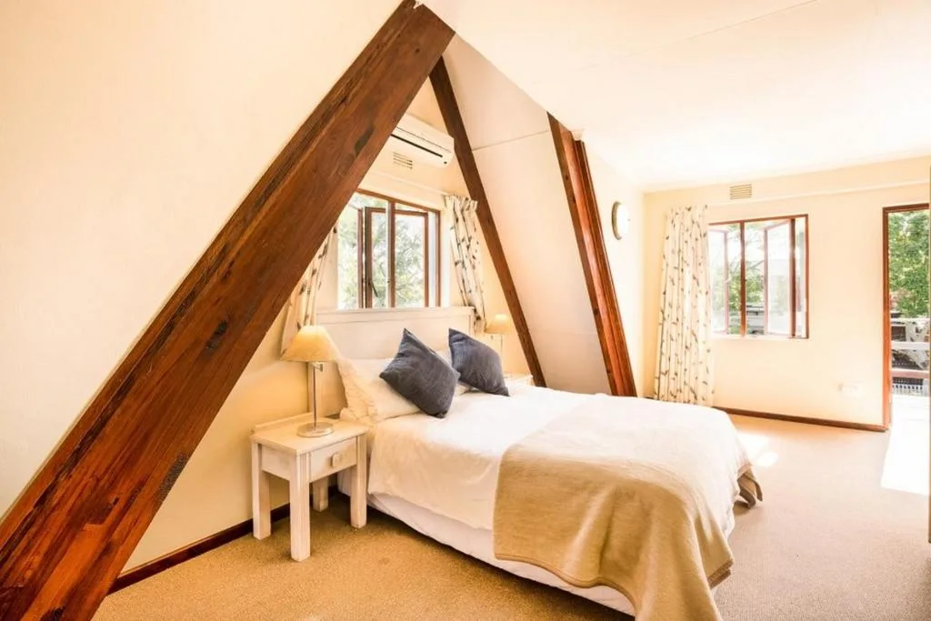 Bright bedroom with exposed wooden beams and queen bed with dark pillows