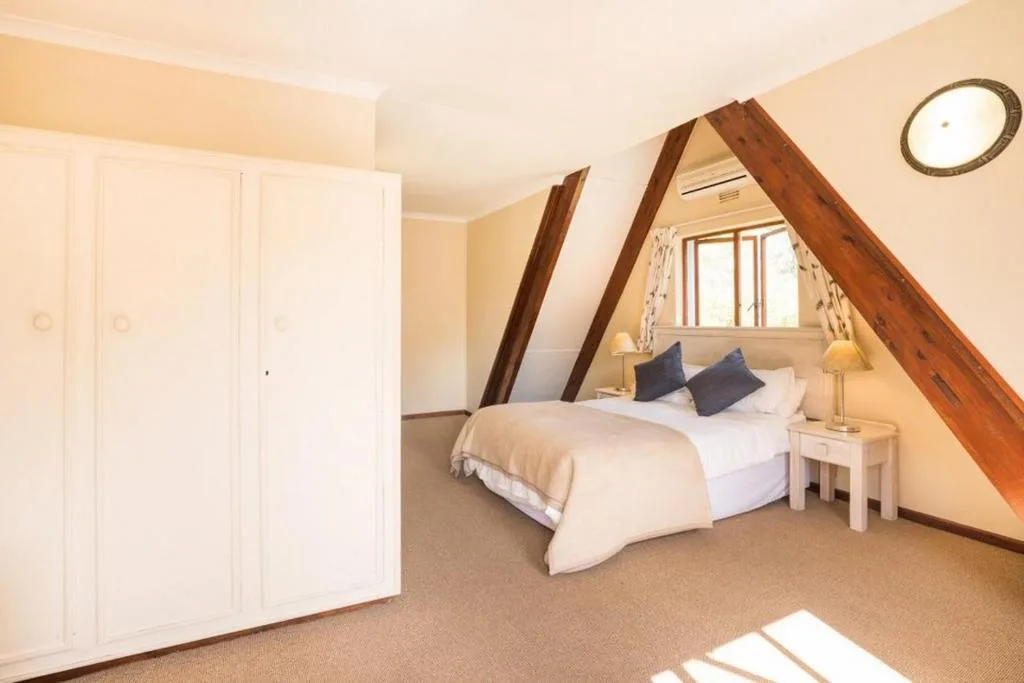 Loft bedroom with sloped timber beams, double bed, and natural light