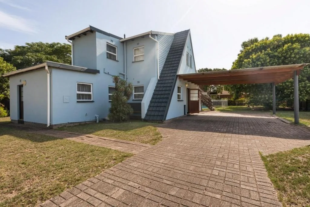 Modern white house with carport and brick paved driveway surrounded by trees