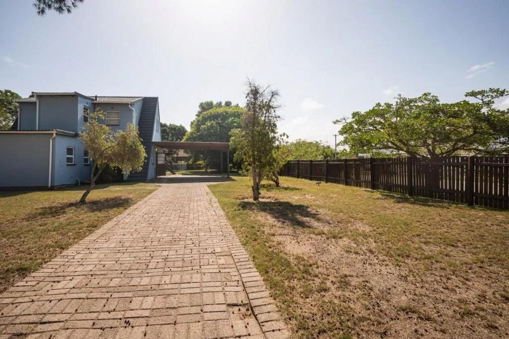 Modern blue house with brick driveway and mature trees, fenced garden