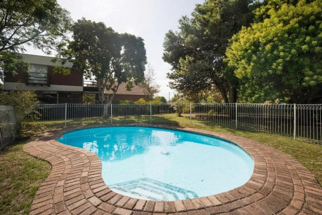 Curved kidney-shaped swimming pool with brick paving and safety fencing
