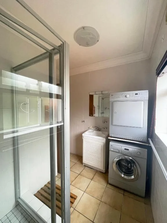 Bathroom with shower enclosure, vanity sink, and stacked laundry appliances
