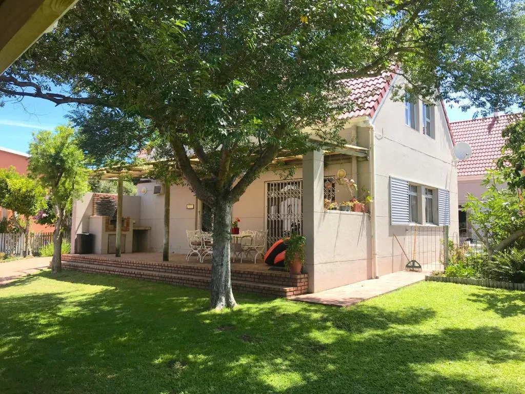 Cream cottage with red tile roof, mature trees, and manicured lawn garden
