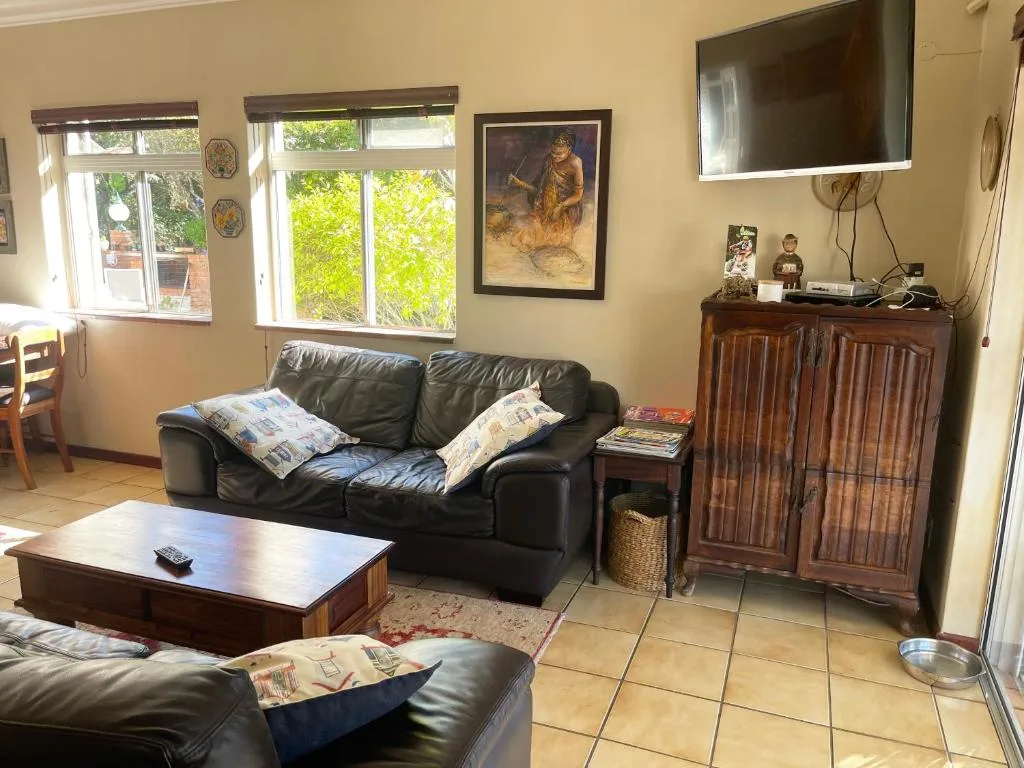 Spacious lounge with black leather sofas, wooden cabinet, and garden views
