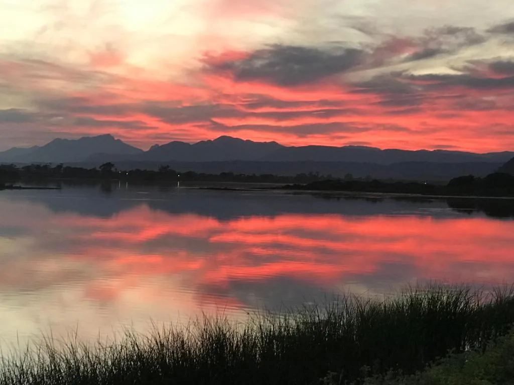 Stunning sunset over lagoon with mountains and dramatic red sky reflected in water