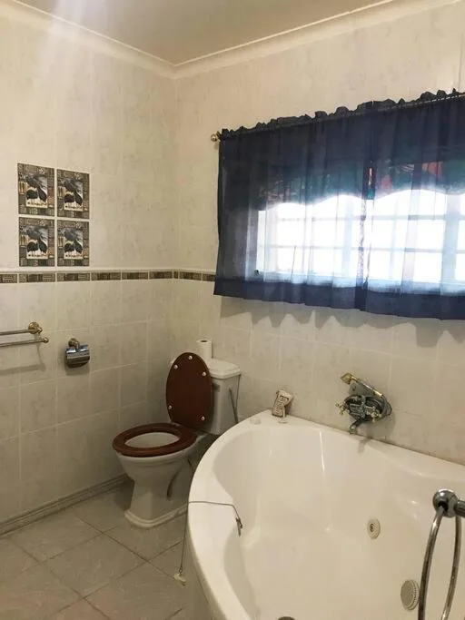 Bathroom with bathtub, toilet, and small window with dark curtains
