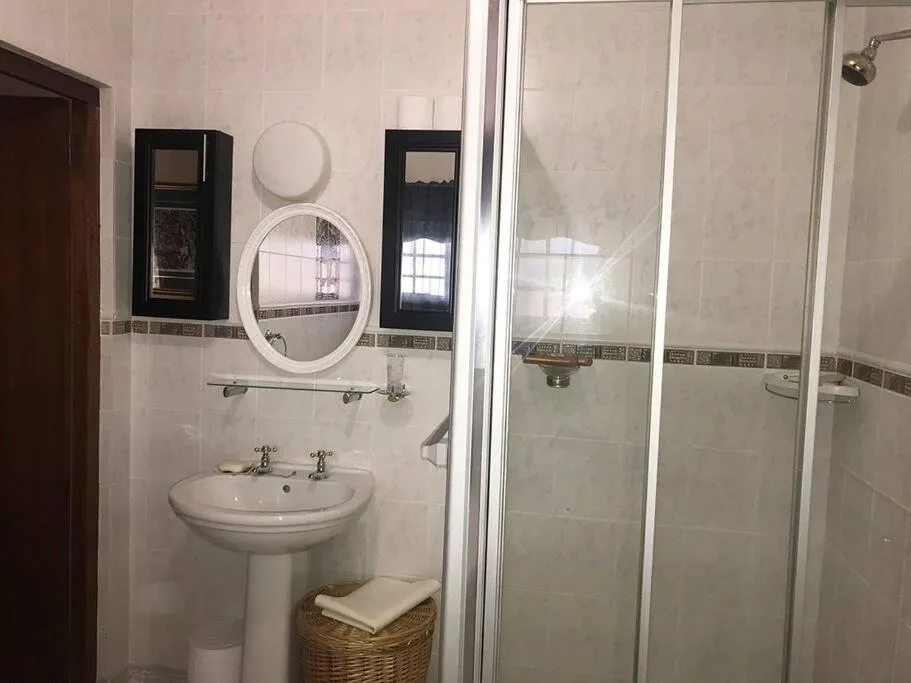 Clean bathroom with pedestal sink, round mirror, and enclosed shower cubicle
