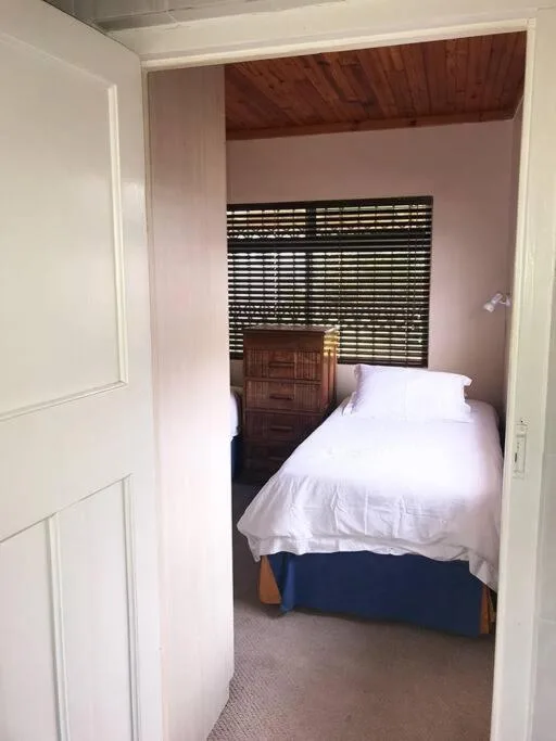Bedroom with white bedding, wooden bedside table, and black louvered window