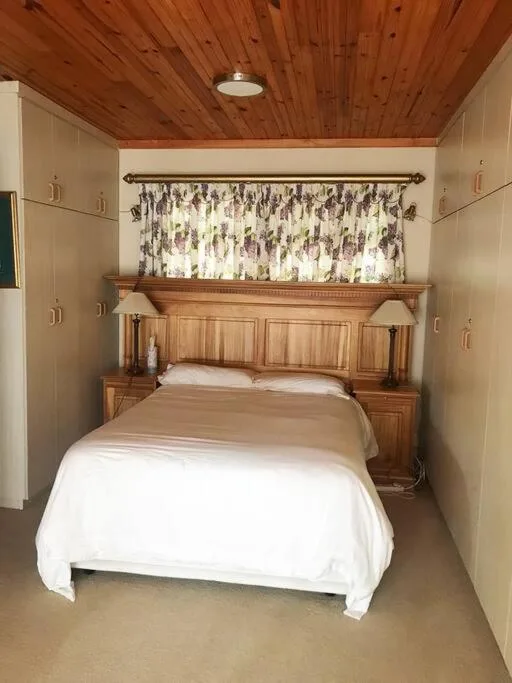 Wooden bed with white bedding in compact bedroom with pine ceiling