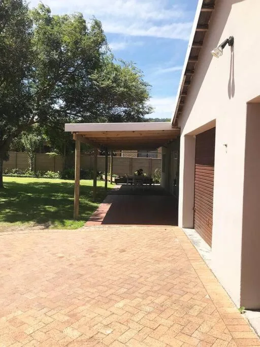 Wooden pergola over brick patio with green lawn and trees