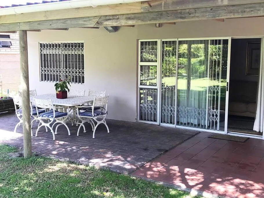 Covered patio with dining table, chairs, and garden views through large sliding doors
