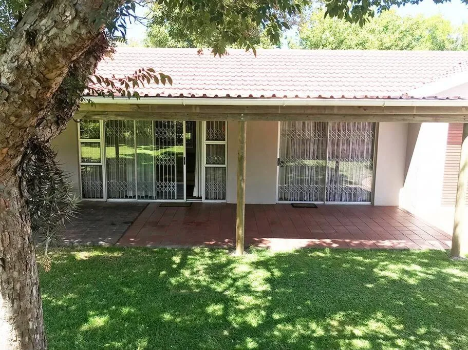 Single-story cottage with covered deck, large windows, and manicured lawn