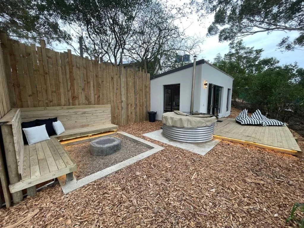 Outdoor patio area with wooden seating, fire pit, and modern white building