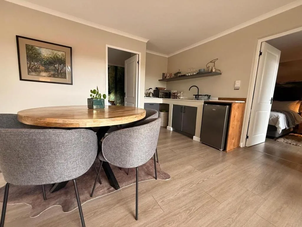 Modern round wooden dining table with gray upholstered chairs and kitchen area beyond