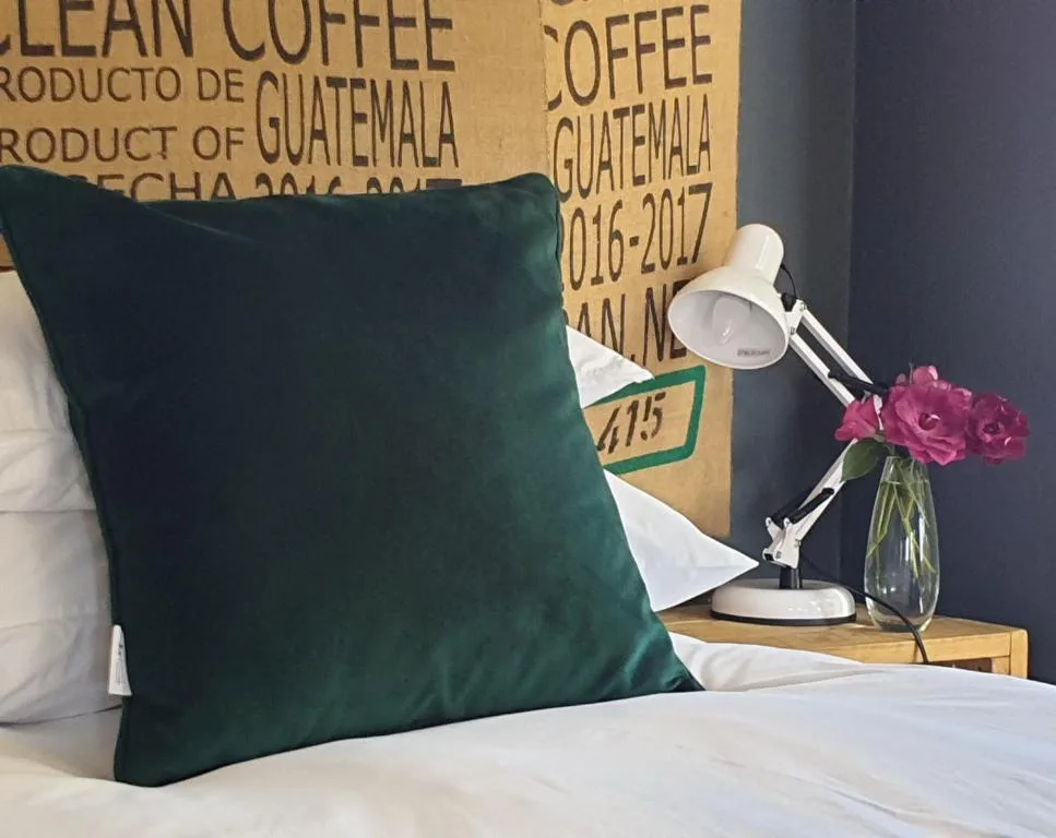 Bedroom detail with green velvet pillow, reading lamp, and fresh flowers