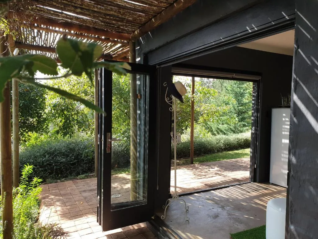 Covered patio with open glass doors overlooking lush garden and hedges