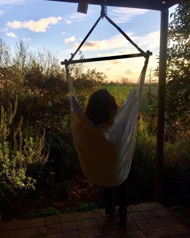 Person relaxing in hanging chair suspended from pergola with countryside views